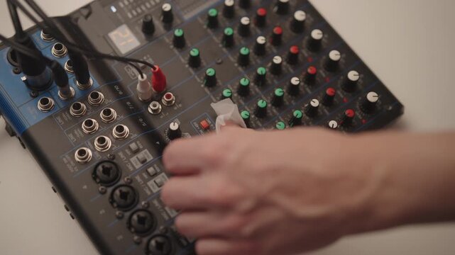 Top view of unrecognizable person cleaning audio mixing console with soft cloth, removing dust from knobs and faders to ensure proper functionality and prolong life of sound production equipment.