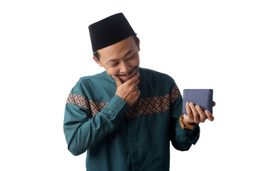 Pensive young Asian Muslim man holding a wallet with an excited expression, thinking about what to buy during Ramadan or before Eid Mubarak. Isolated on a white background, Shopping, budgeting concept