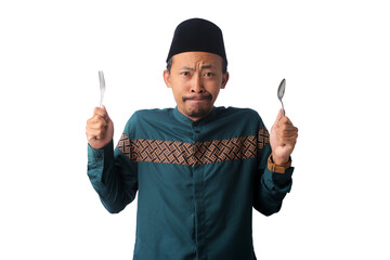 Sad Asian Muslim man wearing a green Indonesian baju koko and songkok cap, looking at the camera with a sad expression while waiting to break his fast during Ramadan, Isolated on a white background