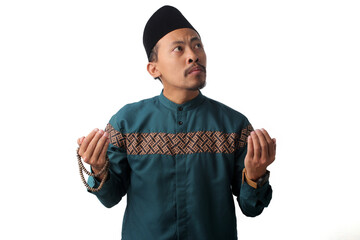 Serious Asian Muslim man wearing traditional Indonesian Muslim clothing, raising his hands in a Muslim prayer gesture while making dua during the Ramadan month, Isolated on a white background