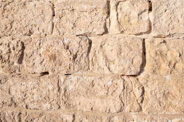 Rough ochre-colored natural stone wall with strong texture and a rusted garage door, captured as a raw architectural and material detail Birżebbuġa, Malta, 6 DEC 2025.