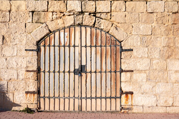 Rough ochre-colored natural stone wall with strong texture and a rusted garage door, captured as a raw architectural and material detail Birżebbuġa, Malta, 6 DEC 2025.