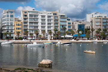 Blue coastline of Il-Gżira with high apartment blocks, small boats and a busy bay, capturing a lively and slightly chaotic Mediterranean holiday atmosphere Il-Gżira, Malta, 9 DEC 2025.
