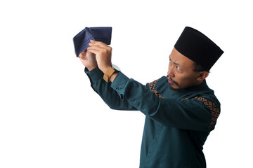 Sad Asian Muslim man wearing traditional Indonesian Muslim attire, a baju koko and black peci (songkok), holding an empty wallet, Isolated on a white background, budgeting, or personal finance concept