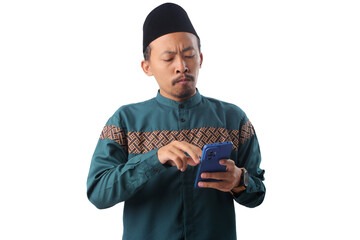 Unhappy Indonesian Muslim man in a green baju koko and black peci (songkok) reacting to his phone with a worried, displeased expression, isolated on a white background.