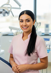 Young smiling Latinx female dentist in a dental office. Handsome doctor in a pink uniform