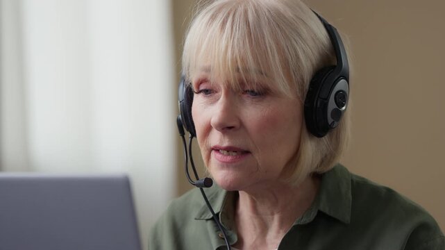 Concentrated senior Caucasian woman talking video call with headset laptop at home serious old businesswoman mature retired business lady online teacher in headphones talk conference virtual discuss