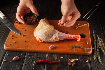 A chef seasons a turkey leg on a wooden board. Ingredients like garlic and herbs are placed nearby. A knife rests at the side, ready for use