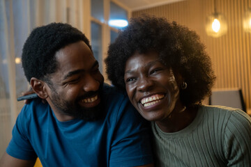 Obraz premium Happy laughing Black couple bonding while relaxing sitting on sofa