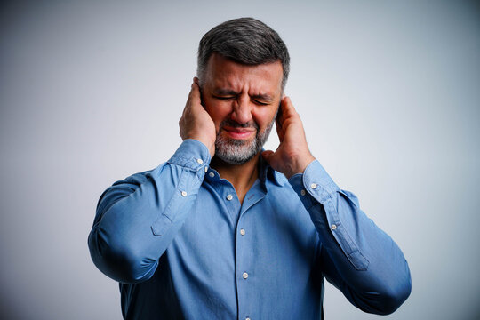 Mature man experiencing tinnitus, holding ear, isolated on white background