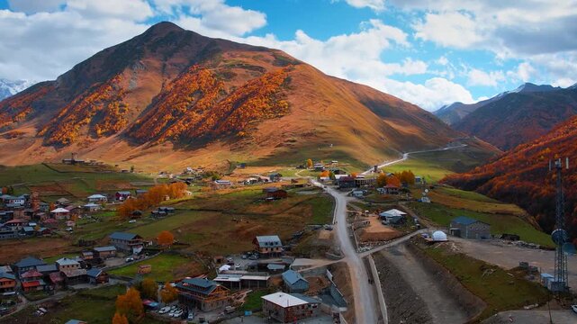 Flight over the picturesque old village with medieval towers in the Caucasian Mountains. Orange woods cover the rocks. Ushguli, Upper Svaneti, Georgia.