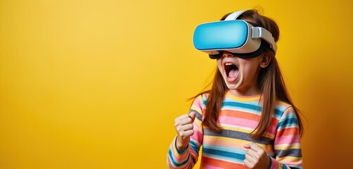 Girl wears VR headset with excitement, hands clenched in victory. Child experiences virtual reality with amazement and joy. Colorful stripes on shirt contrast yellow background.