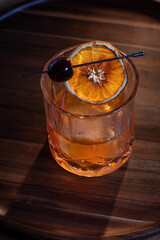 whiskey cocktail served on the rocks garnished with a dehydrated orange slice with dramatic lighting served on a wooden surface.