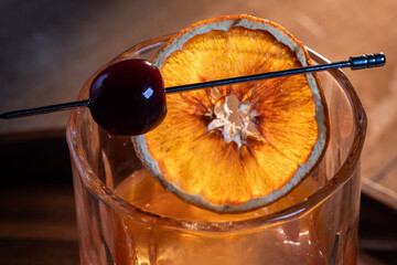 Beautiful garnish of a dehydrated orange slice and a dark cherry on a whiskey cocktail served on the rocks.