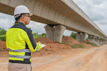 An Asian male engineer works at a motorway bridge construction site,Civil worker inspecting work on crossing construction,Supervisor working at high-speed railway construction site