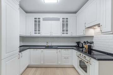 A kitchen features white cabinets with glass doors and a black countertop. Cooking tools and...