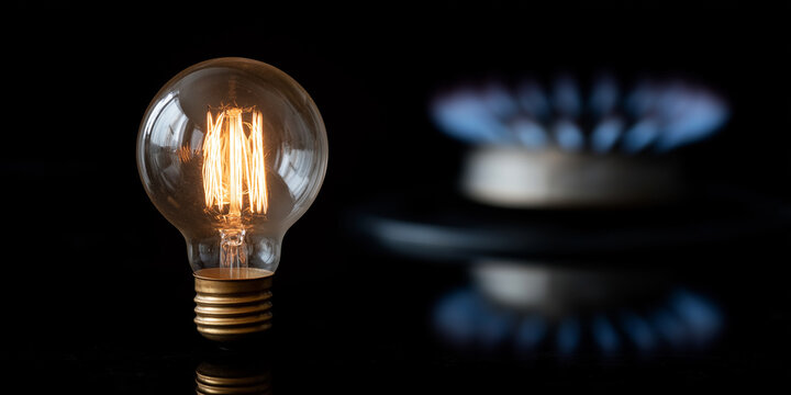 Glowing filament light bulb beside a blue gas flame, symbolizing energy cost, consumption, and utility choices