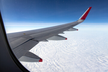 View of an aircraft's wing and engines in flight, from a passenger window. Perspective is looking down towards a dense blanket of white, puffy clouds, a high altitude. Engine covers red-tipped cones.