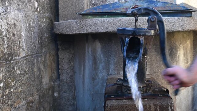 Drawing water from a well using a traditional cast iron hand pump.