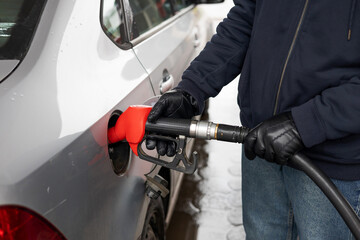 Filling a car with gasoline, hands with a hose at a gas station close-up.