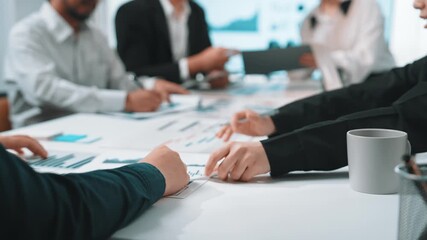 A diverse business team collaborates in a modern office meeting, analyzing graphs and discussing strategies using digital devices and documents on the table. SACTR - Powered by Adobe