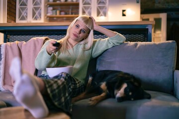 Obraz premium Lazy Evening at Home – Bored Woman with Remote Control and Dog