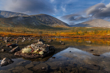 Autumn Lake Scene With Mossy Rocks, Calm Water, and Mountain Backdrop