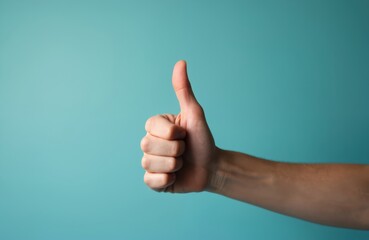 Hand shows thumbs up sign against light blue background. Positive gesture indicates agreement or success. Great for approval themes in marketing.