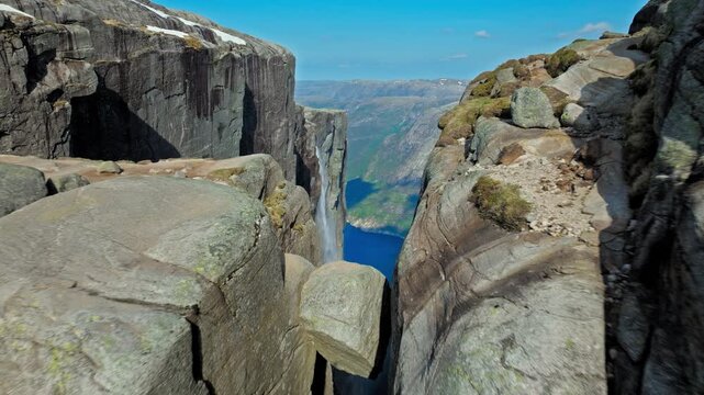 Kjeragbolten rock wedged between cliffs above Lysefjord Norway. Aerial drone view shows the famous suspended boulder framed by steep granite walls and deep fjord far below on a clear summer day.