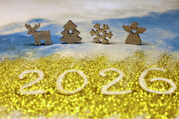 A Christmas scene with four wooden figures and the blurred number 2026 written in glitter. The scene is festive and joyful, with the snowflakes and the angel symbolizing the holiday season