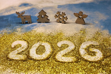 A gold glittery background with four wooden figures of a deer, a tree, an angel, and a snowflake. The numbers 2026 are written in white on the background