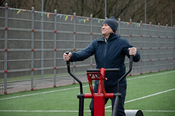 Caucasian senior male 60s resting on outdoor fitness equipment, staying active and maintaining healthy lifestyle during workout session. Outdoor Fitness Workout