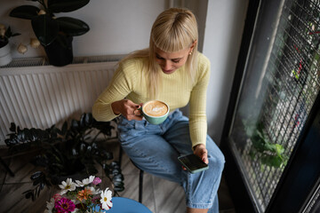 Woman relaxing in cafe drinking coffee and using phone