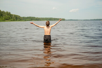 Person stands waist-deep in a lake with arms wide open, embracing nature. Visible expression of freedom and joy. Forested shorelines create a serene environment, highlighting peace.