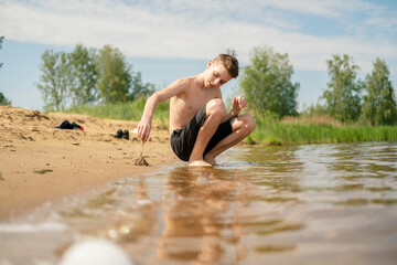 Fototapeta premium Young boy enjoying sunny day at lakeside, playing in the sand and water. The scene conveys a sense of joy and freedom, capturing the essence of childhood fun in nature.