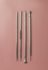 Metal tools for cleaning skin with acne or blackheads. Needles for closed comedones on a pink background.
