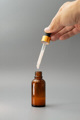 Glass bottle with skin serum or other substance on a gray background, vertical image