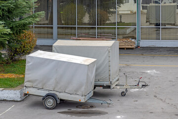 Two Small Cargo Trailers With Grey Canopy Parked Behind Building