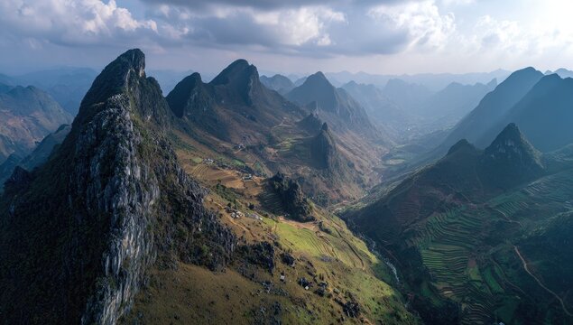 Panoramic view of rugged mountain peaks and valleys under a cloudy sky; landscape with trails