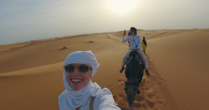 Group of tourists journey through the expansive Sahara Desert, riding camels and capturing memorable moments