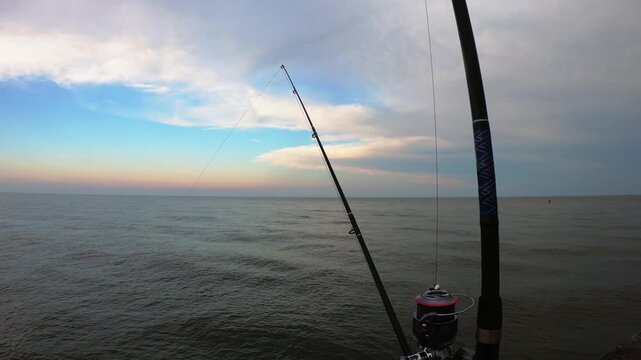 Fishing with rods overlooking calm waters under a colorful evening sky