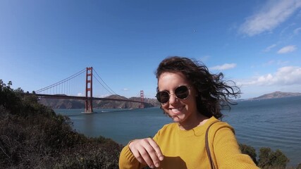 Woman taking selfie standing on hill with panoramic view of Golden Gate Bridge on a sunny day in San Francisco