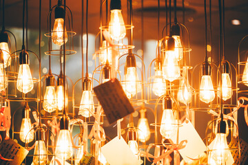 Festive New Year decor with glowing Edison bulb in metal cage, hanging pendant light on cord with ribbon and wish tag, warm golden bokeh illumination for party interior