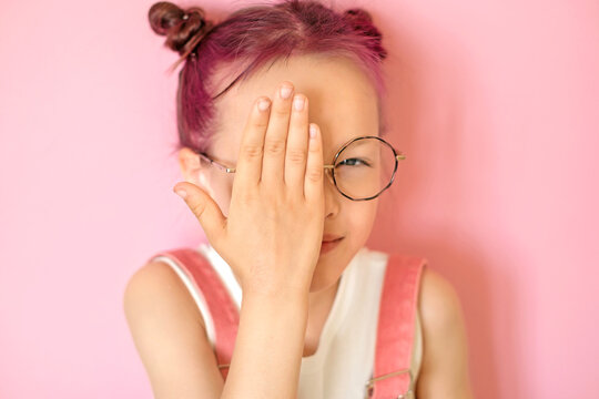 A child with glasses squints and tries to concentrate his vision with left eye, covering his right hand. Correction and treatment of vision