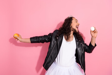 Homosexual nonbinary man in a leather jacket wearing a ballet dress, posing playfully on a pink pastel background
