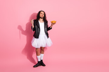 Gay nonbinary man in a tutu and leather jacket on a pink backdrop expresses bold style and pride through cake moment and playful pose © deagreez