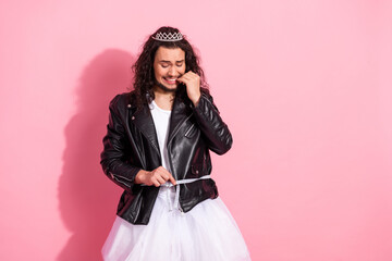 Non-binary LGBT man in a leather jacket and tutu measures waist against pink pastel background, celebrating individuality and fashion