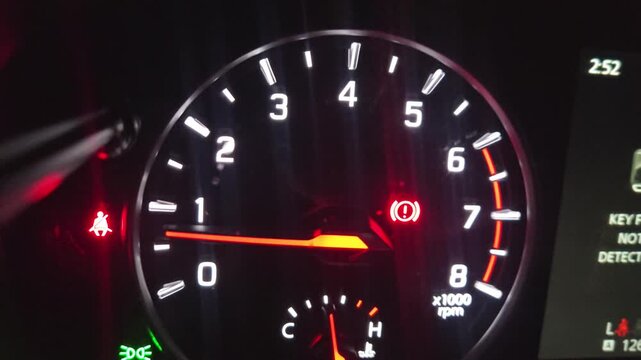 Close-up view of an automobile instrument cluster displays speed, engine RPM, warning indicators, and digital navigation information in low-light conditions.