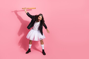 Playful nonbinary LGBT dancer in tutu and leather jacket strikes a dynamic pose with a baseball bat on pink backdrop