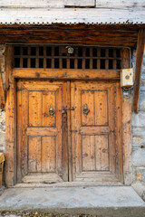 A traditional double-winged wooden door of a historic stone house, featuring rice-grain hammered and hand-carved motifs.